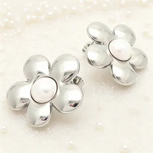 Détail de boucles d'oreilles fleur argentée avec perle sur fond blanc scintillant.