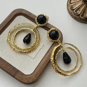 Close-up of golden textured metal earrings with black resin teardrops on a wooden stand