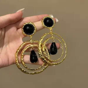 Close-up of vintage gold hammered earrings with black resin teardrops and triple hoop design