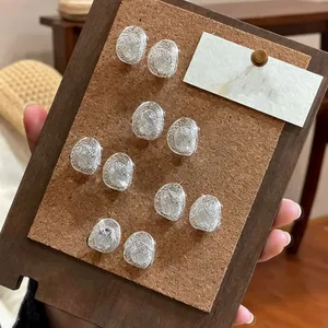 Detailed view of intricate silver hollow mesh oval stud earrings on a wood cork board