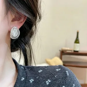 Close-up of elegant silver hollow mesh oval stud earrings worn by a model.