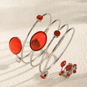 Close-up of silver spiral bangle and ring set with red gemstones on textured background.