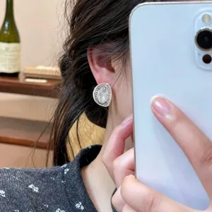 Close-up detail shot of an elegant silver hollow mesh oval stud earring worn on the ear