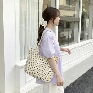 Model carrying a cream canvas tote bag with black polka dots and patch detail