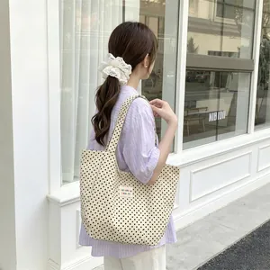Back view of a woman carrying a large polka dot canvas tote bag near a shop window