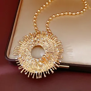 Dettaglio macro di una collana dorata con ciondolo a sole, strass e un motivo ad ape