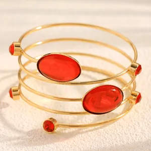 Close-up of a layered gold spiral bangle with oval red resin gemstones and rhinestones