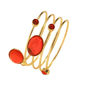 Detailed macro view of a gold-tone spiral wrap bangle featuring vibrant red oval gemstones