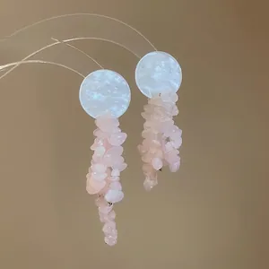 Gros plan sur des boucles d'oreilles bohèmes en pierre rose avec disque en nacre blanc