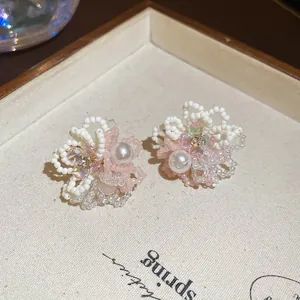 Détail rapproché de boucles d'oreilles fleurs en perles roses et blanches sur plateau beige