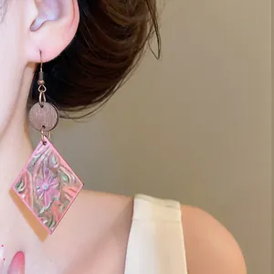 Primer plano de pendientes de madera en forma de rombo con estampado floral rosa en modelo.