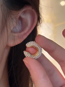 Close-up detail of a vintage C-shape ear cuff with white pearls held near the ear for scale