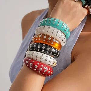 Primo piano di bracciali in resina colorati con rivetti in metallo argento lucido impilati.