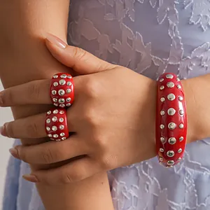Primo piano di un elegante set di bracciale e anelli in resina rossa con borchie argentate