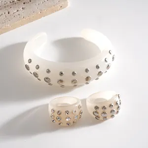 Dettaglio di un set di gioielli in resina crema con borchie metalliche e cristalli lucenti.