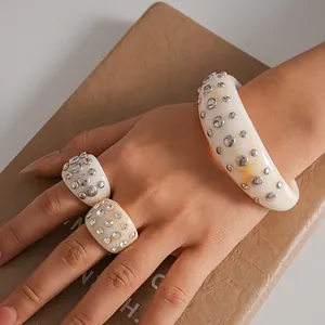 Primo piano di set di gioielli in resina bianca con borchie metalliche e strass sulla mano