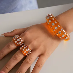 Dettaglio di anelli e bracciale in resina arancione con borchie argentate tonde.