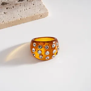 Dettaglio ravvicinato di un anello in resina ambrata con molti strass bianchi brillanti