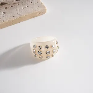 Dettaglio di un anello in resina color crema con strass scintillanti incastonati