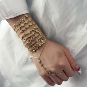 Close-up of layered gold charm bracelets with Hand of Fatima and sun pendants on wrist.