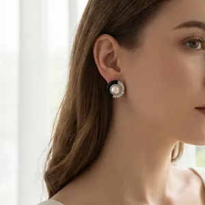 Gros plan élégant d'une boucle d'oreille en résine noire et perle sur une femme.