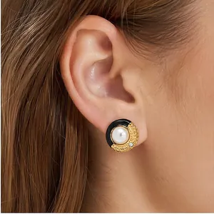 Gros plan sur une boucle d'oreille en émail noir et or avec perle de coquillage.
