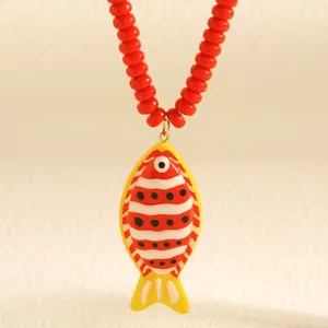 Détail d'un collier de perles rouges orné d'un pendentif en forme de poisson tropical.