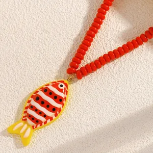 Gros plan d'un pendentif poisson tropical sur un collier de perles rouges de plage.