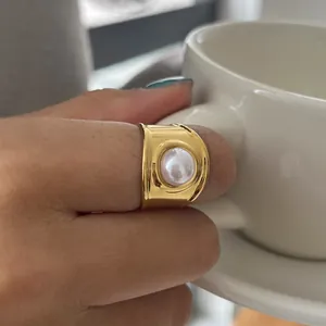 Primo piano di un anello in acciaio inossidabile dorato con perla centrale.