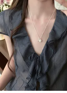 Close-up of a silver popcorn pendant necklace on a model wearing a ruffled blouse