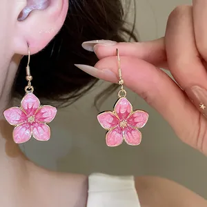 Close-up detail of pink enamel cherry blossom ear hooks with shimmering star centers