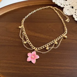 Detailed view of a sweet pink enamel flower pendant on a layered gold chain necklace