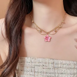Detailed close-up of a sweet pink enamel flower pendant on a layered gold chain.