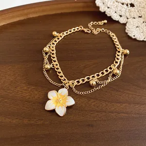 Close-up detail of a gold layered charm bracelet featuring a white enamel plumeria flower
