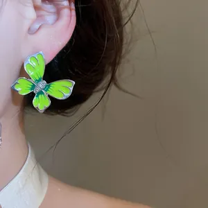 Close-up detail of a vibrant green enamel butterfly stud earring with crystal center