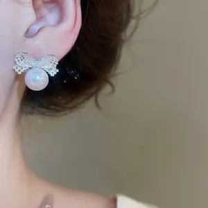 Close-up of elegant silver bow stud earrings with a dangling white pearl on model.