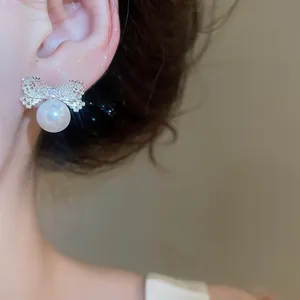 Elegant silver bow stud earring with large white pearl pendant shown on model ear