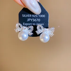 Close-up view of elegant silver bow earrings featuring white pearls and zircon details