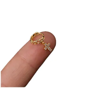 Pendiente de aro dorado para cartílago con dije de cruz de circonitas en el dedo