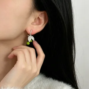 Close-up of green cherry and leaf earrings worn on ear with sparkling cubic zirconia