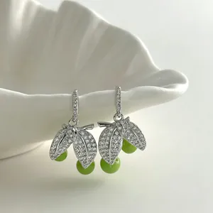 Close-up of elegant leaf-shaped earrings with zircons and green beads on a white shell