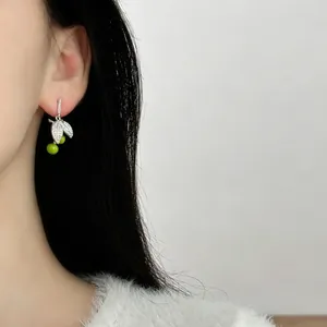 Detailed macro shot of elegant silver needle cherry earrings with zircon leaves on model.