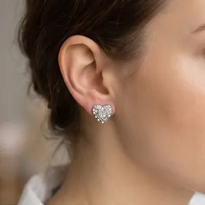 Close-up of sparkling heart-shaped stud earrings with pavé stones on a model's ear