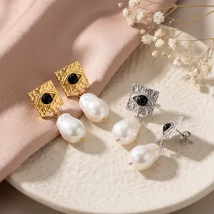 Close-up of square evil eye earrings with dangling baroque pearls in gold and silver.