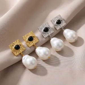 Detail of evil eye square earrings with large baroque pearl drops in gold and silver.