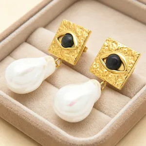 Close-up of golden evil eye earrings with dangling baroque pearls in a velvet box