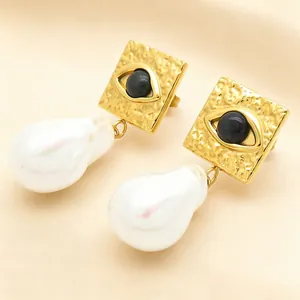 Detailed view of gold square devil's eye earrings with large white baroque pearl drops