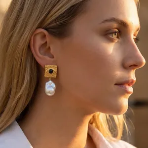 Close-up detail of evil eye stainless steel earrings with baroque pearl drop on model.