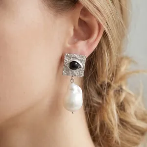 Detailed view of square evil eye earring with a large white baroque pearl drop charm