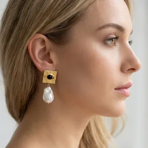 Detailed view of a vintage gold evil eye earring with a white baroque pearl on model.